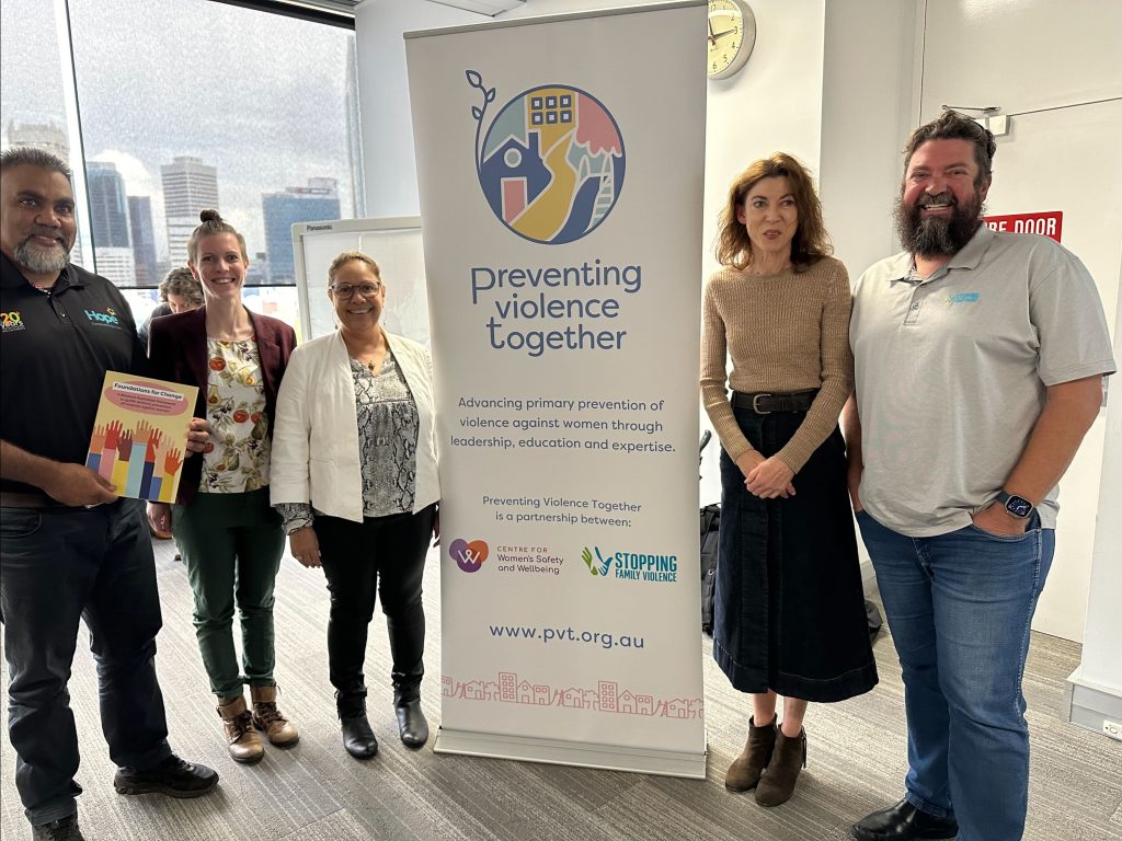 Photo of five people standing next to a Preventing Violence Together banner. One person is holding a copy of Foundations for Change.